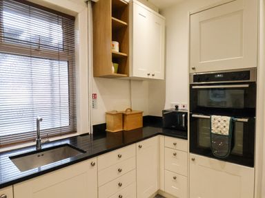 A kitchen with white cabinets black countertop a built in oven microwave sink and window with blinds at South Bay Beach House Bridlington