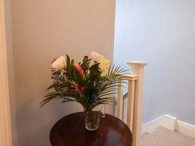 A bouquet of flowers in a glass vase on a round wooden table next to a staircase at South Bay Beach House in Bridlington