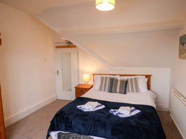 A bedroom with a double bed with striped pillows bedside table with lamp and folded towels on bed at South Bay Beach House in Bridlington