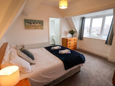 A bedroom with a bed pillows lamp chest of drawers and window at South Bay Beach House in Bridlington