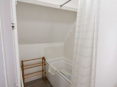 A bathroom with a white bathtub with a shower curtain and a wooden towel rack next to it at South Bay Beach House in Bridlington