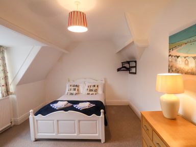 A bedroom with a white bed and pillows a wooden dresser with a lamp and a painting on the wall at South Bay Beach House in Bridlington