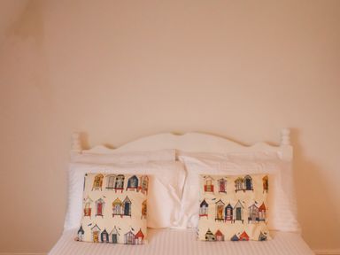 A bed with a white headboard two white pillows and two pillows with a colorful beach hut pattern at South Bay Beach House Bridlington