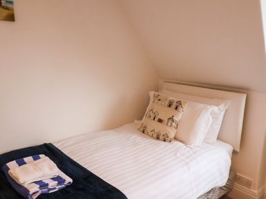 A single bed with white bedding and decorative pillows against a white wall at South Bay Beach House in Bridlington