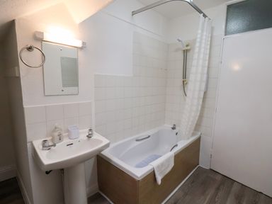 A bathroom with a bathtub with shower curtain a pedestal sink mirror and a closed door at South Bay Beach House in Bridlington