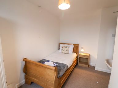 A small bedroom with a wooden single bed a nightstand with a lamp and a wall-mounted sink at South Bay Beach House in Bridlington