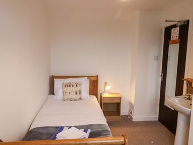 A small bedroom with a single bed a pillow a bedside table with a lamp a door with a mirror and a sink at South Bay Beach House in Bridlington