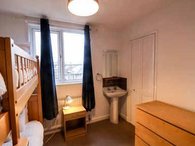 A bedroom with bunk beds a wooden nightstand and lamp a sink with a mirror and a wooden dresser at South Bay Beach House Bridlington