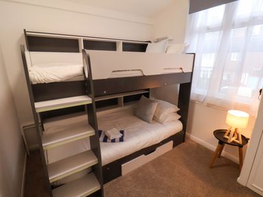 A bedroom with a bunk bed stairs a small round table with a lamp and a window with curtains at South Bay Beach House Bridlington
