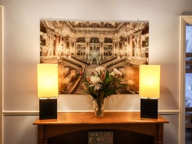 A wooden mantelpiece with two rectangular lamps and a vase of flowers below a large ornate framed picture at South Bay Beach House Bridlington