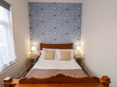 A bedroom with a wooden bed frame white bedding two beige pillows two bedside tables with lamps and a window with curtains at South Bay Beach House in Bridlington