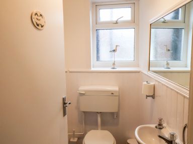 A small bathroom with a toilet sink mirror and window with a bird decoration at South Bay Beach House in Bridlington
