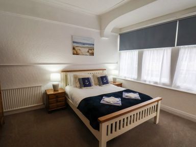 A bedroom with a double bed with navy bedding two bedside tables with lamps and three windows with blue blinds at South Bay Beach House in Bridlington