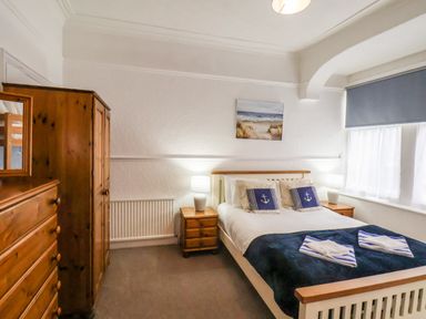 A bedroom with a double bed and wooden furniture including a wardrobe and chest of drawers at South Bay Beach House in Bridlington