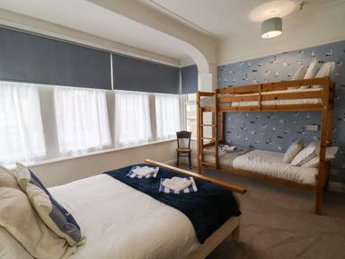 A bedroom with a double bed, bunk beds, a chair, and windows with blinds at South Bay Beach House in Bridlington