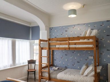 A bedroom with a wooden bunk bed a chair and windows with blue blinds at South Bay Beach House in Bridlington