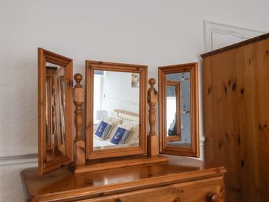 A wooden dresser with a three-panel vanity mirror reflecting a bed with nautical themed cushions at South Bay Beach House in Bridlington