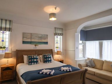 A bedroom with a wooden bed with pillows and folded towels a beige sofa by a window with curtains and two bedside tables with lamps at South Bay Beach House in Bridlington