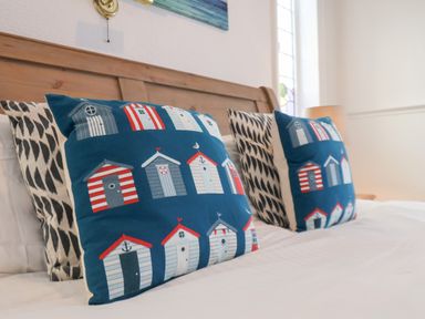 Two decorative pillows with beach hut designs on a bed with a wooden headboard at South Bay Beach House in Bridlington
