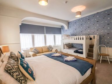 A bedroom with a double bed, bunk beds, a sofa, and a chair with blue patterned wallpaper at South Bay Beach House in Bridlington