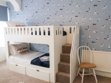 A bedroom with a white bunk bed and stairs beside a white chair with wooden seat at South Bay Beach House in Bridlington