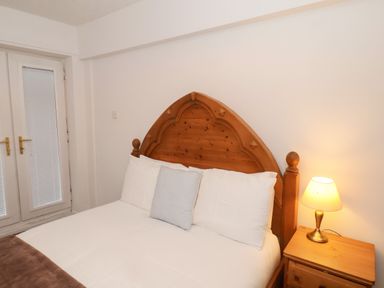 A bedroom with a wooden bed frame pillows a bedside table with a lamp and a door with blinds at South Bay Beach House in Bridlington