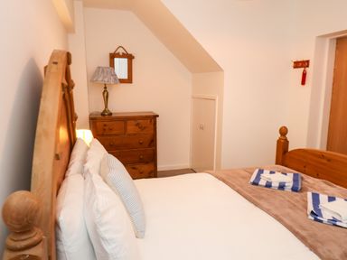 A bedroom with a wooden bed and headboard a wooden chest of drawers a lamp and a small wall mirror at South Bay Beach House in Bridlington
