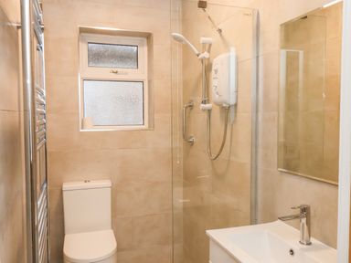 A bathroom with a white toilet a shower with a glass door a sink with a faucet a mirror and a frosted window at South Bay Beach House in Bridlington
