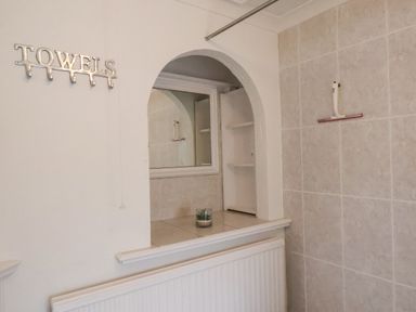 A bathroom wall with towel hooks and an arched opening with shelves and a small plant at South Bay Beach House in Bridlington