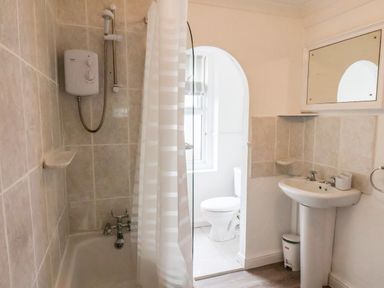 A bathroom with a bathtub shower combination a white sink with a mirror above and a toilet visible through an arched doorway at South Bay Beach House in Bridlington