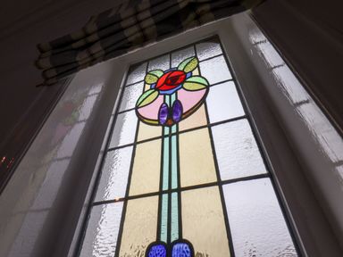 A stained glass window with colorful floral pattern and a curtain above it at South Bay Beach House in Bridlington