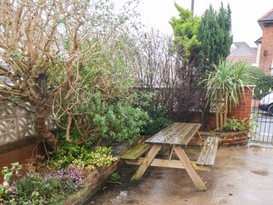 A wooden picnic table on a wet patio surrounded by various plants and small trees at South Bay Beach House in Bridlington