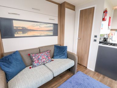 A living room with a sofa and cushions next to a wooden door and kitchen area at Balvicar Beag Balvicar Isle Of Seil