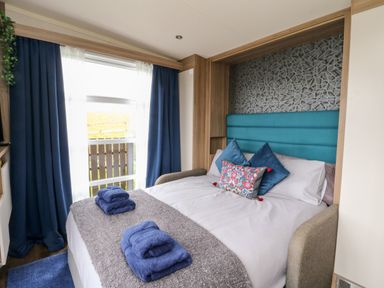 A bedroom with a bed with folded towels on it and blue curtains at Balvicar Beag in Balvicar Isle Of Seil
