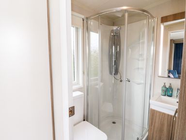 A bathroom with a corner shower cabin a toilet a sink with two soap dispensers and a mirror at Balvicar Beag in Balvicar Isle Of Seil