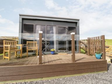 A wooden deck with two chairs and a table by a glass door at Balvicar Beag in Balvicar Isle Of Seil