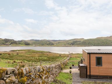 A view of a grassy field with grazing cows by a body of water and hills in the background at Balvicar Beag Balvicar Isle Of Seil