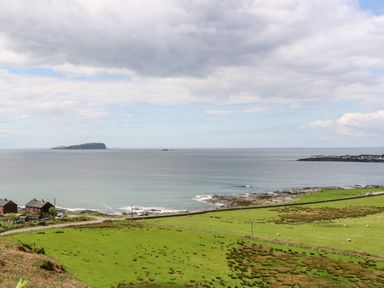 A coastal view with green fields sheep houses and an island in the sea at Balvicar Beag Balvicar Isle Of Seil