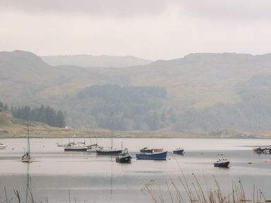 Boats anchored on calm water with hills and trees in the background at Balvicar Beag in Balvicar Isle Of Seil