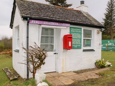 A small white building with a tiled roof a red post box and signs outside Balvicar Beag Balvicar Isle Of Seil