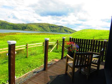 A wooden deck with two chairs and a flowerpot overlooking a green field and hills at Balvicar Beag in Balvicar Isle Of Seil