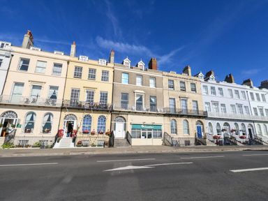 A row of multi-colored buildings with balconies and flowers at 123 On The Sea – Victoria’s Place in Weymouth