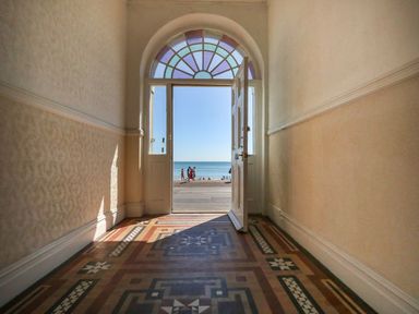 A hallway with an open door leading to the ocean at 123 On The Sea – Victoria’s Place in Weymouth