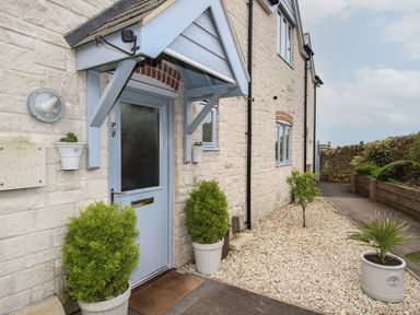 Front door entrance with a blue door and plants in pots on a gravel path at Blue Waters in Weymouth