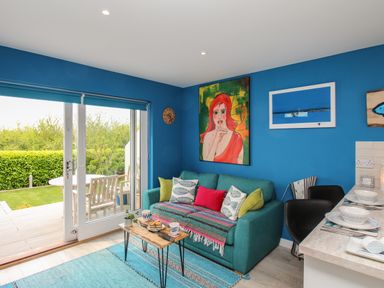 A living room with a blue sofa and colorful cushions and a small wooden table next to a glass door leading to a garden at Blue Waters in Weymouth