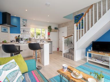 An open plan kitchen and living area with bar stools at a counter a staircase and a television at Blue Waters in Weymouth