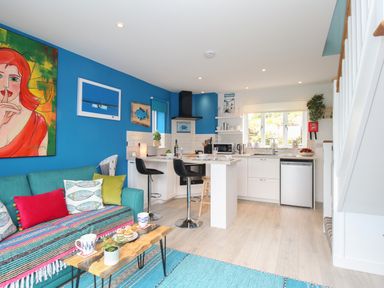 An open plan living room and kitchen with a teal sofa and colorful cushions at Blue Waters in Weymouth