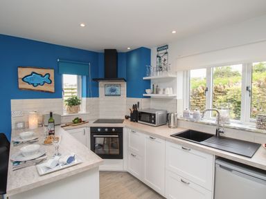 A kitchen with white cabinets blue walls a black oven and countertop appliances at Blue Waters in Weymouth