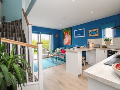 An open living area with a striped carpeted staircase blue walls a couch and a kitchen bar at Blue Waters Weymouth