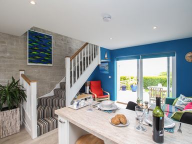 A kitchen island with plates and wine bottle and a staircase with striped carpet by a blue wall with sliding glass doors at Blue Waters in Weymouth